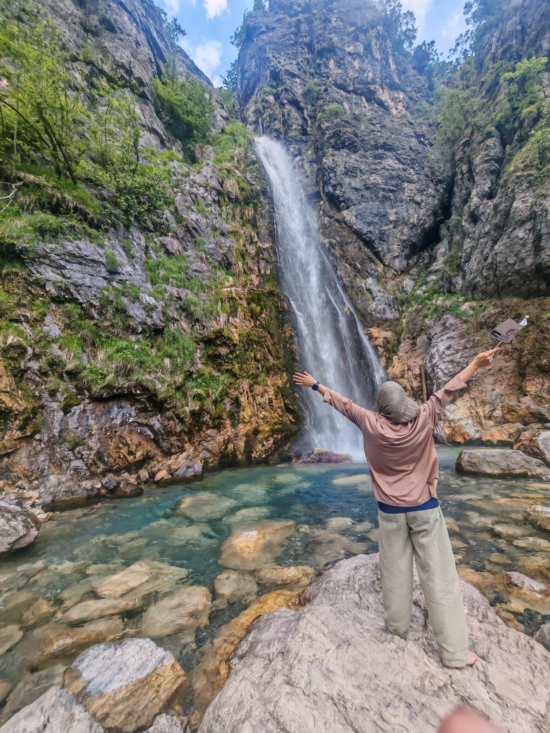 A sister with arms outstretched in front of a mountain waterfall