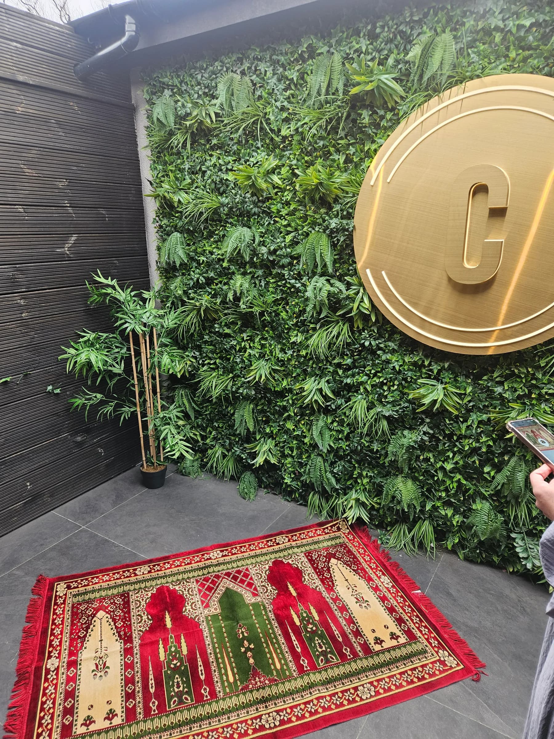 A prayer mat laid out beside a green plant wall