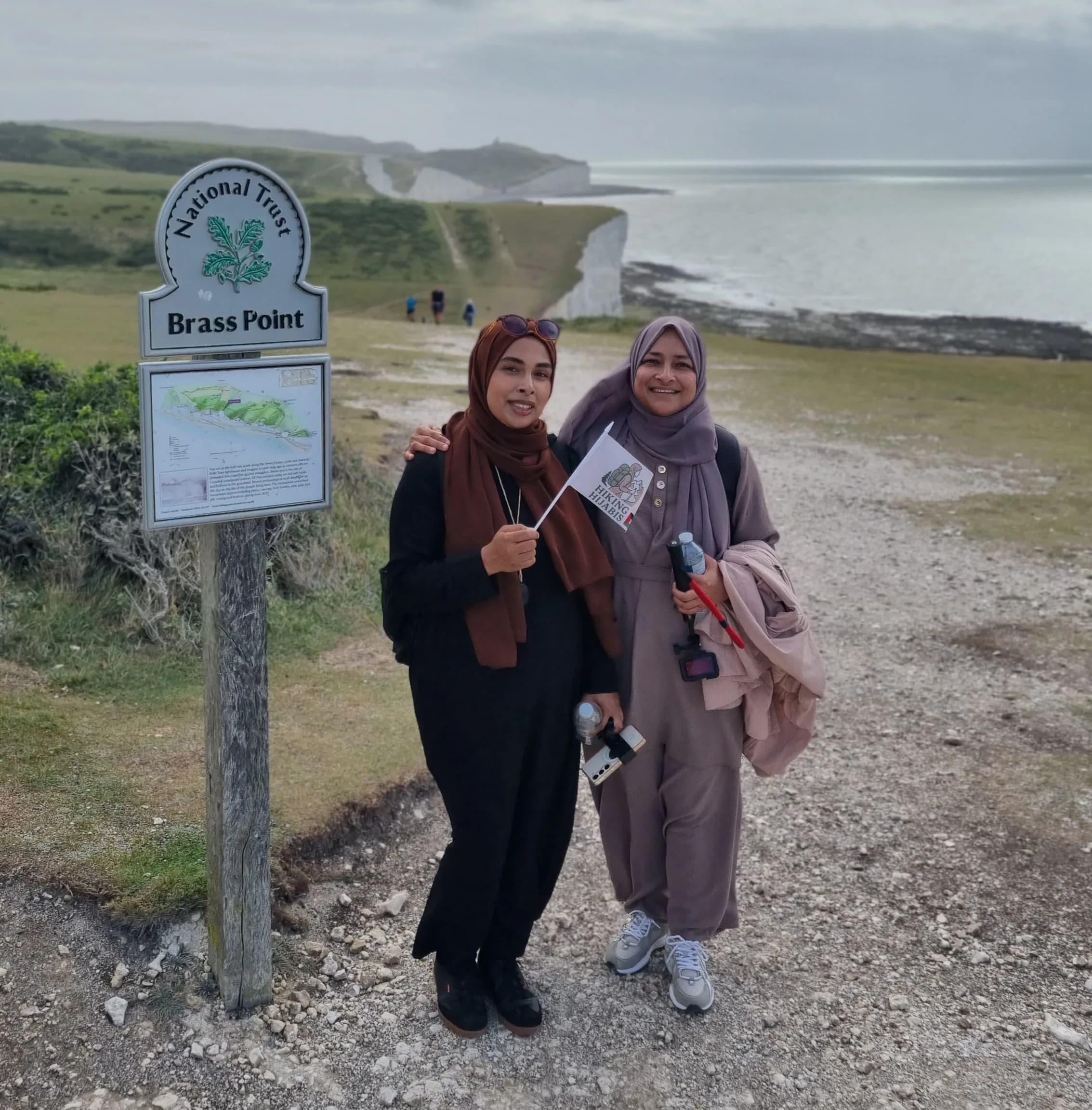Two sisters beside the Brass Point National Trust sign, with the Seven Sisters cliffs behind